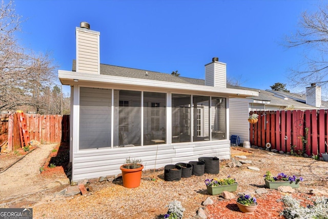 back of house with a sunroom, a fenced backyard, and a chimney