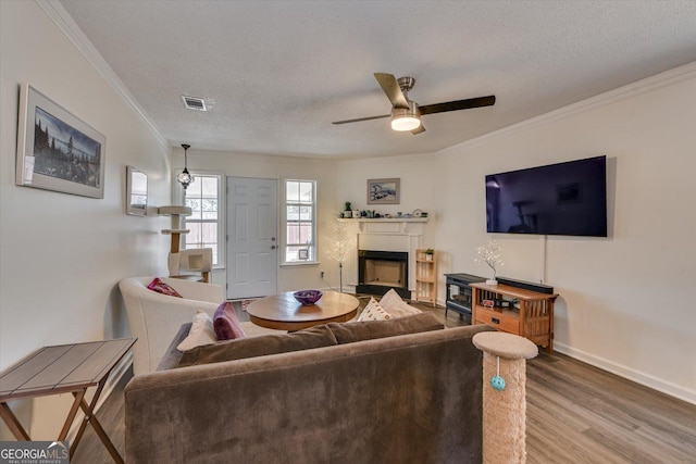 living room with visible vents, wood finished floors, a textured ceiling, crown molding, and a fireplace