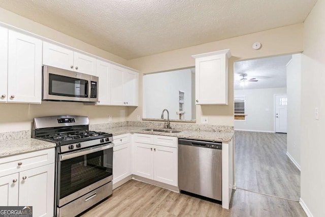 kitchen featuring light stone countertops, stainless steel appliances, light wood-style floors, white cabinetry, and a sink