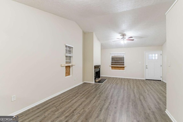 unfurnished living room featuring light wood-type flooring, baseboards, a fireplace with raised hearth, and a textured ceiling