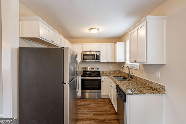 kitchen featuring dark wood-style flooring, appliances with stainless steel finishes, white cabinetry, a sink, and dark stone counters