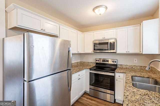 kitchen with stainless steel appliances, white cabinets, a sink, and light stone countertops