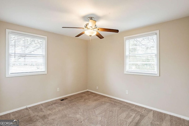 carpeted empty room with a healthy amount of sunlight, baseboards, visible vents, and ceiling fan