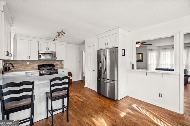 kitchen with appliances with stainless steel finishes, a breakfast bar, light countertops, white cabinetry, and a sink