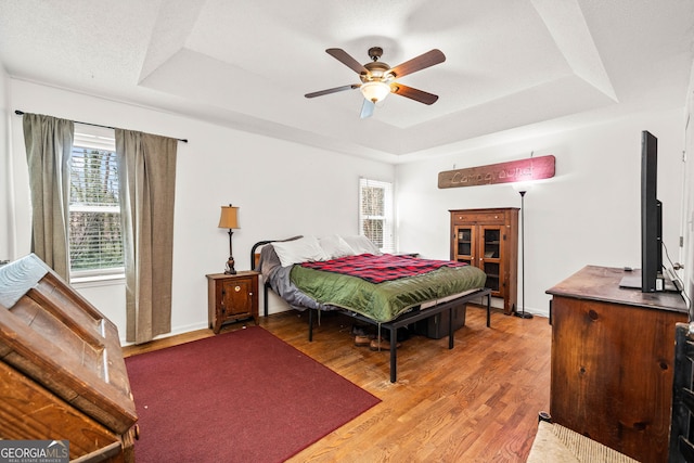 bedroom with a raised ceiling, ceiling fan, light wood-style flooring, and baseboards