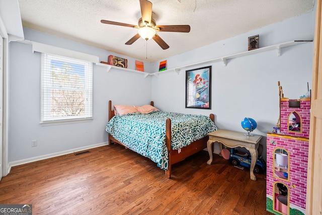 bedroom featuring baseboards, visible vents, a ceiling fan, wood finished floors, and a textured ceiling