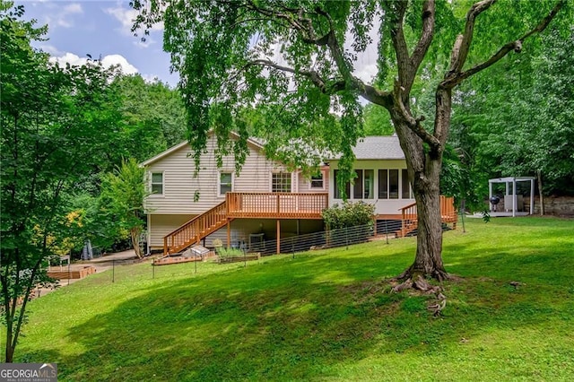 back of house featuring fence, a sunroom, stairs, a lawn, and a wooden deck