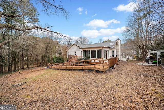 back of property with a sunroom, a chimney, and a deck