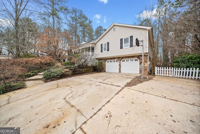 view of property exterior featuring a garage, concrete driveway, stone siding, and fence