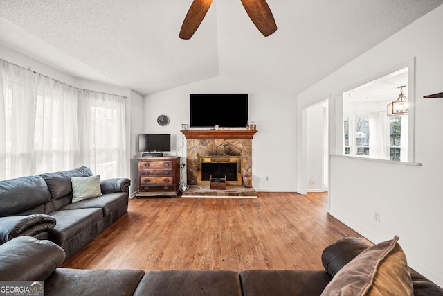 living room featuring baseboards, wood finished floors, vaulted ceiling, a textured ceiling, and a fireplace