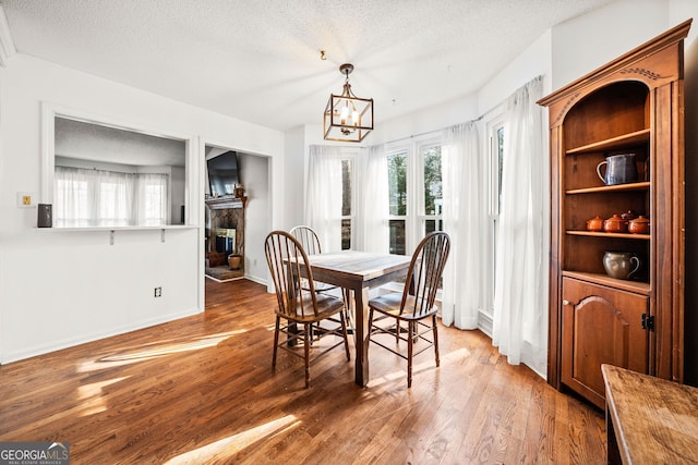 dining area with a fireplace, a textured ceiling, an inviting chandelier, and wood finished floors