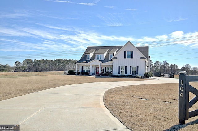 view of front facade featuring board and batten siding, driveway, a front lawn, and fence