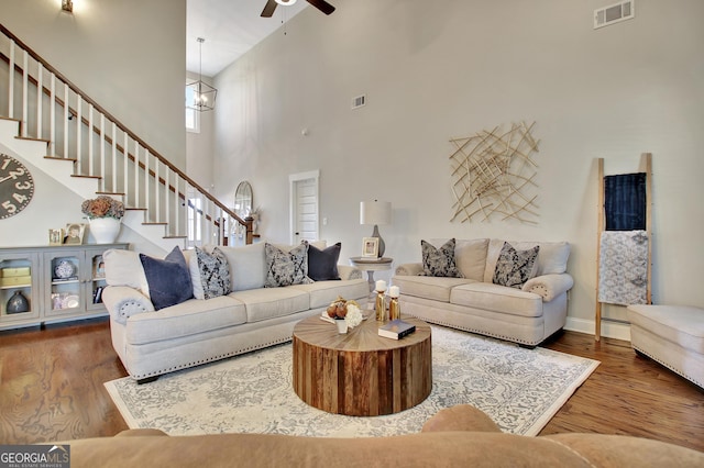 living room featuring stairs, dark wood-style flooring, ceiling fan with notable chandelier, and visible vents