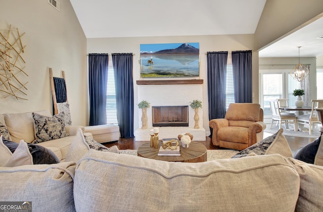 living room featuring lofted ceiling, visible vents, a fireplace with raised hearth, an inviting chandelier, and wood finished floors