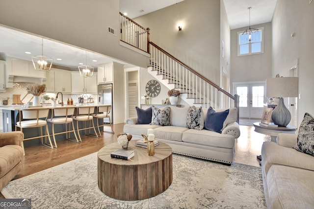 living room with french doors, visible vents, stairway, an inviting chandelier, and light wood-type flooring