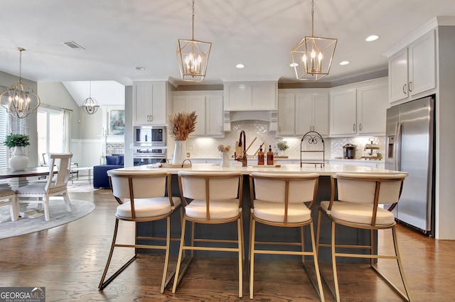 kitchen featuring appliances with stainless steel finishes, an island with sink, and a notable chandelier