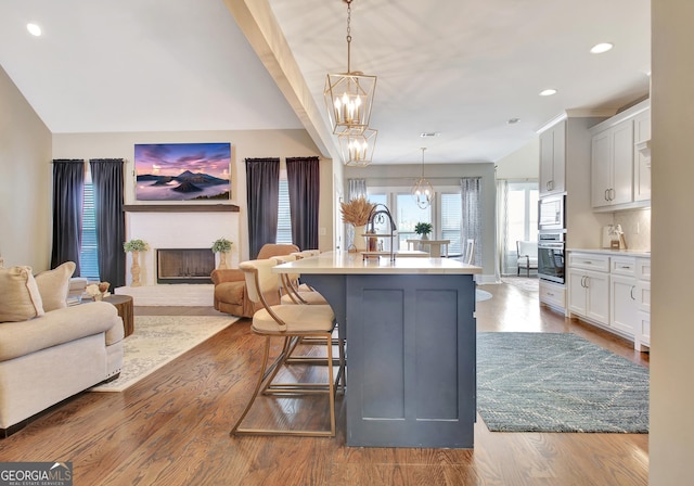 kitchen featuring an island with sink, appliances with stainless steel finishes, open floor plan, hanging light fixtures, and light countertops