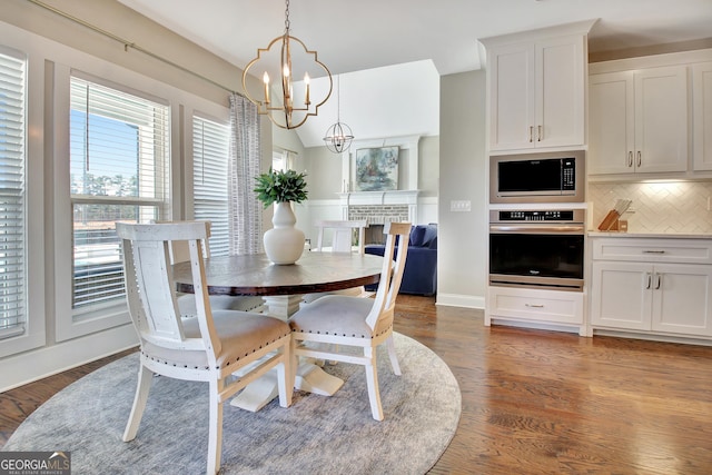 dining room with lofted ceiling, a brick fireplace, dark wood finished floors, and a notable chandelier