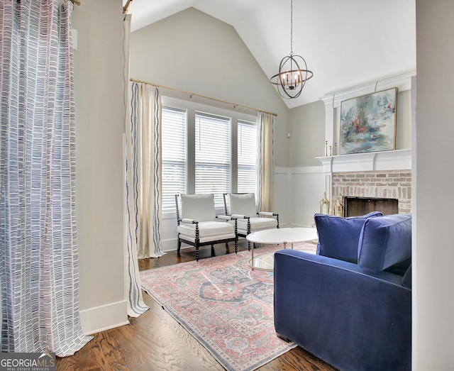 sitting room with a wainscoted wall, wood finished floors, vaulted ceiling, a fireplace, and a notable chandelier