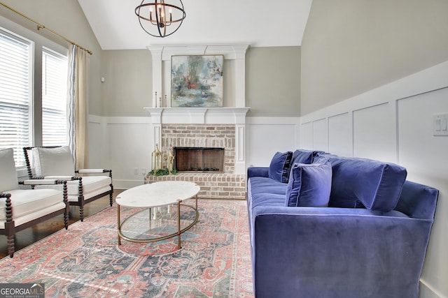 living room with a decorative wall, a brick fireplace, wainscoting, vaulted ceiling, and wood finished floors