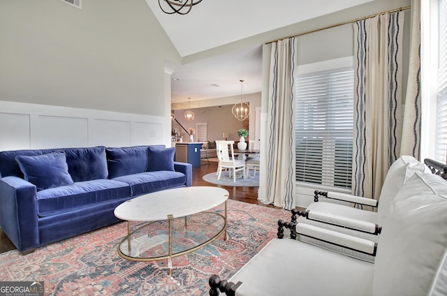 living room with a chandelier, lofted ceiling, wood finished floors, stairs, and wainscoting