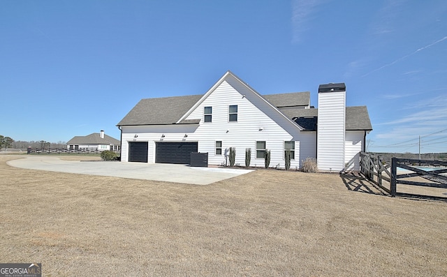 view of side of property featuring fence, concrete driveway, roof with shingles, a lawn, and a chimney