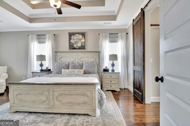 bedroom featuring a tray ceiling, a barn door, ornamental molding, wood finished floors, and baseboards