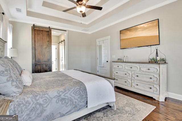 bedroom featuring a barn door, visible vents, dark wood-style flooring, a tray ceiling, and crown molding