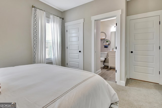 bedroom with light colored carpet, ensuite bath, and baseboards