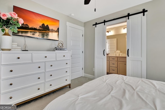 bedroom with light colored carpet, ensuite bathroom, a barn door, ceiling fan, and baseboards