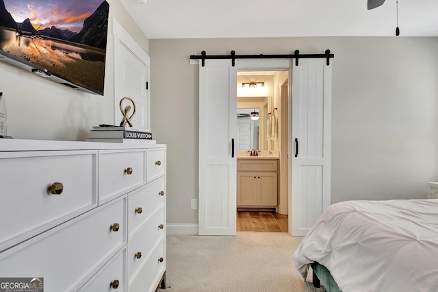 bedroom with light carpet, a barn door, baseboards, connected bathroom, and a sink