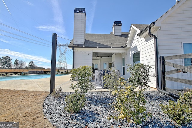 rear view of property featuring a patio, fence, roof with shingles, an outdoor pool, and a chimney