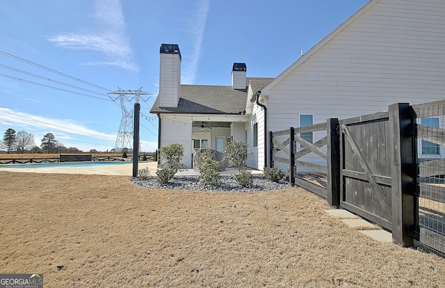 rear view of property with a chimney, a pool, a ceiling fan, a gate, and fence