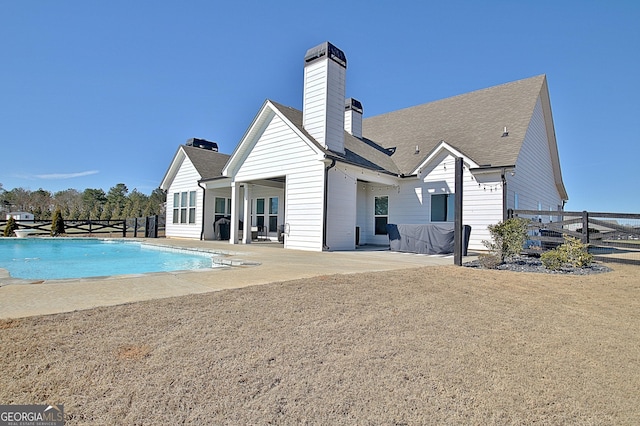 rear view of house with a fenced in pool, a patio, a chimney, a shingled roof, and fence