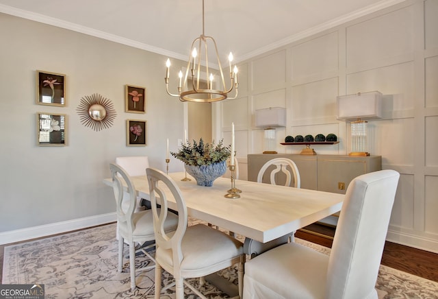 dining space with crown molding, a decorative wall, an inviting chandelier, wood finished floors, and baseboards