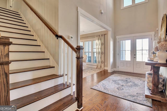 foyer entrance with dark wood-style flooring, a towering ceiling, french doors, stairway, and crown molding