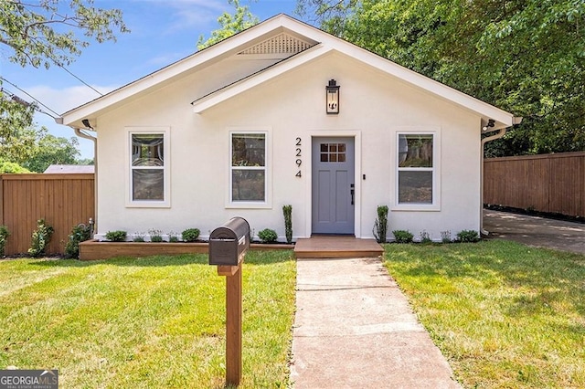 bungalow-style house with a front yard, fence, and stucco siding