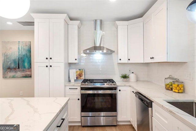 kitchen with stainless steel appliances, wall chimney range hood, and white cabinets