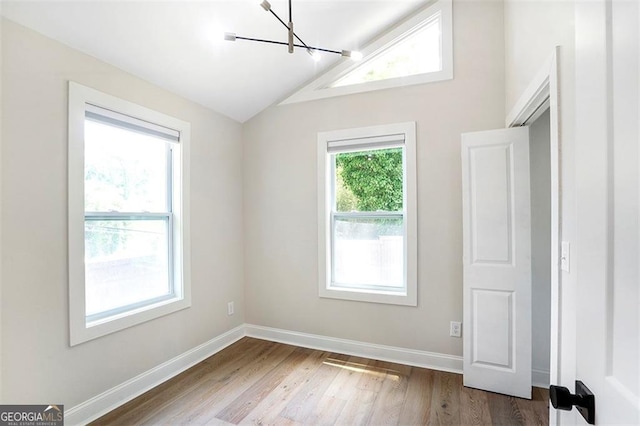 empty room featuring an inviting chandelier, baseboards, vaulted ceiling, and wood finished floors