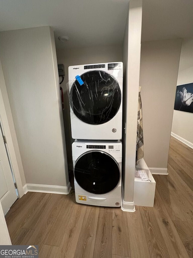 clothes washing area with laundry area, baseboards, wood finished floors, and stacked washer and clothes dryer