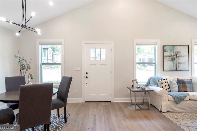 foyer entrance with a chandelier, high vaulted ceiling, light wood-style flooring, and baseboards