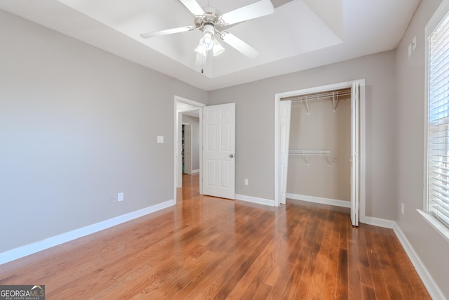 unfurnished bedroom featuring wood finished floors, a closet, a raised ceiling, and baseboards