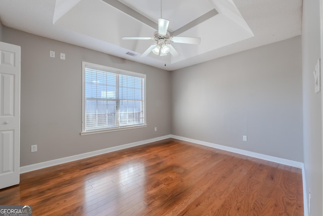 empty room with wood finished floors, a ceiling fan, visible vents, baseboards, and a tray ceiling