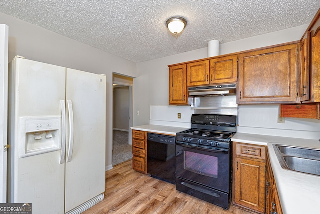 kitchen with under cabinet range hood, light countertops, brown cabinets, black appliances, and light wood finished floors