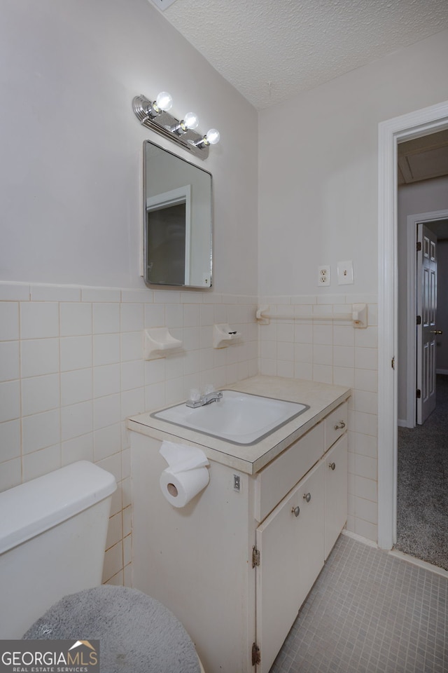 bathroom with a textured ceiling, toilet, a wainscoted wall, vanity, and tile walls