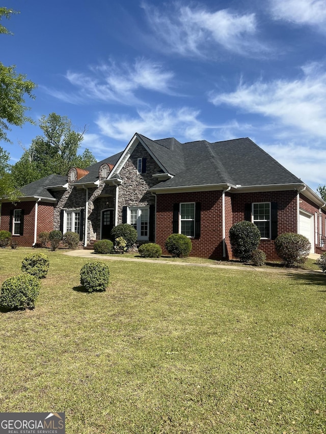 view of front of house with brick siding, an attached garage, a front yard, and roof with shingles