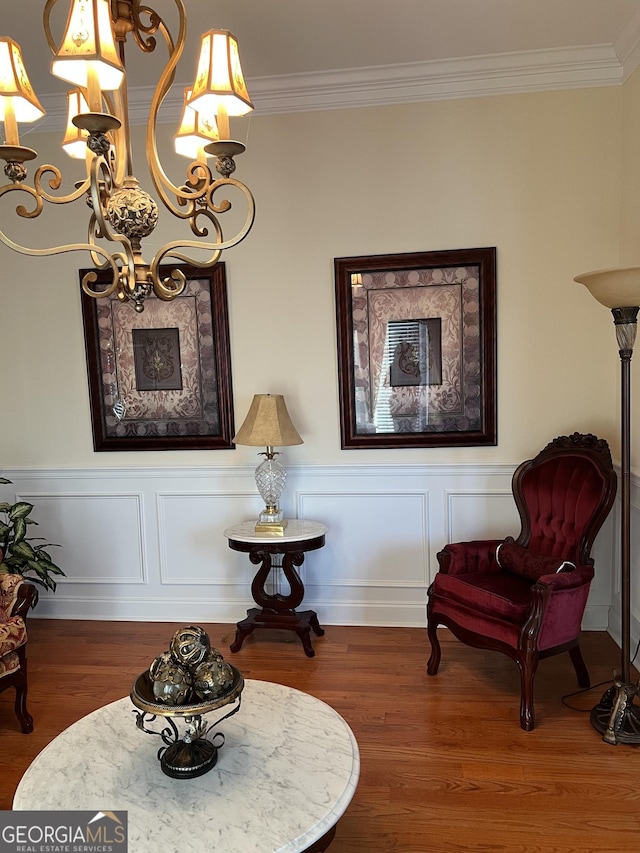 sitting room featuring a notable chandelier, wood finished floors, crown molding, and a wainscoted wall