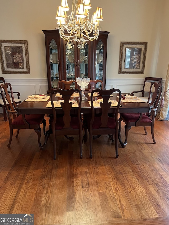 dining area with a chandelier, wood finished floors, a decorative wall, and wainscoting