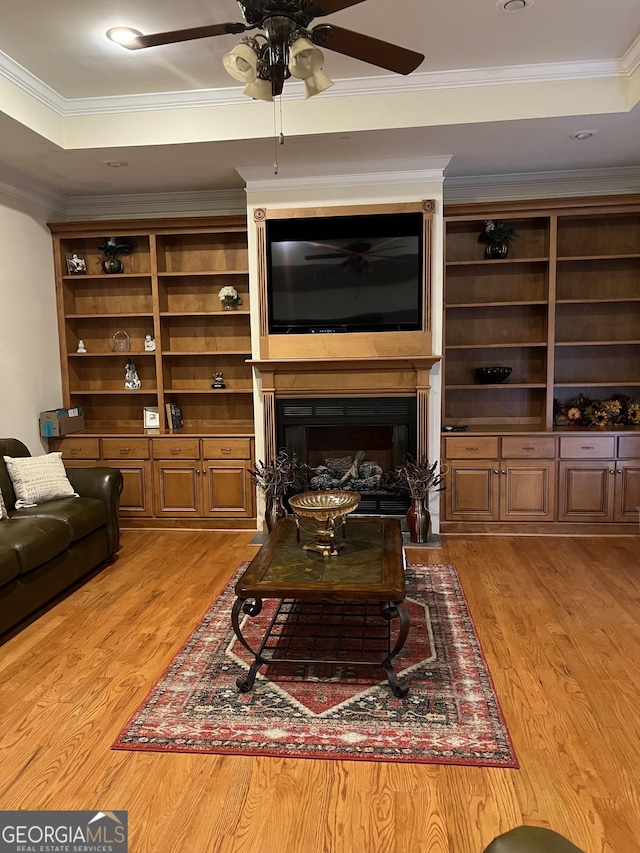 living room featuring light wood finished floors, a ceiling fan, a fireplace, and ornamental molding