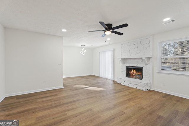 unfurnished living room with visible vents, wood finished floors, a high end fireplace, and a ceiling fan